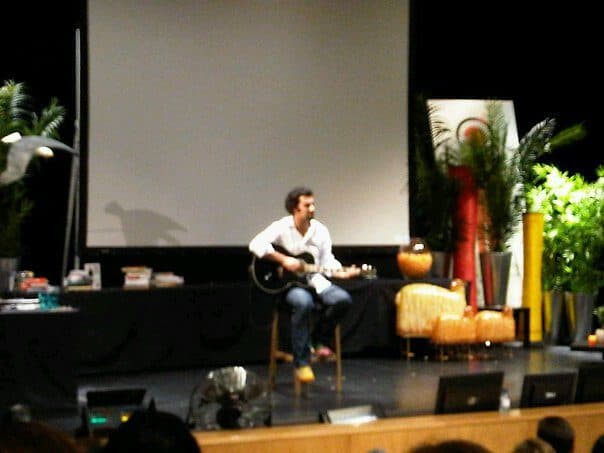 Daniel sentado em palco a tocar guitarra.