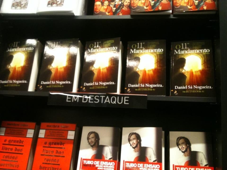 "O 11.º Mandamento" numa prateleira de livraria, sob a etiqueta "Em destaque".