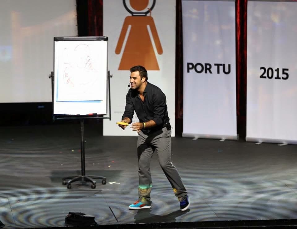 Daniel em palco junto a um quadro de folhas, com o painel "Por Tu 2015" atrás.