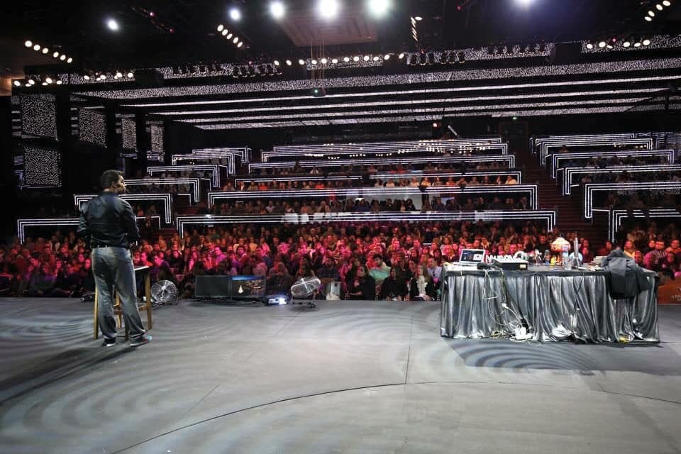 Daniel visto de costas em palco, perante uma arena cheia.